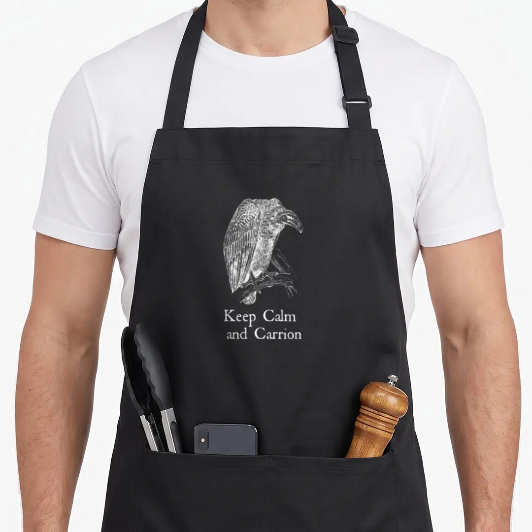 Carrion funny vulture apron - White line-art vulture perched on branch above Keep Calm and Carrion text — shown on a black cotton canvas apron against a white background