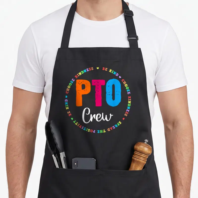 Pto cute teacher apron - PTO Crew text surrounded by multicolored kindness quotes and small hearts — shown on a black cotton canvas apron against a white background