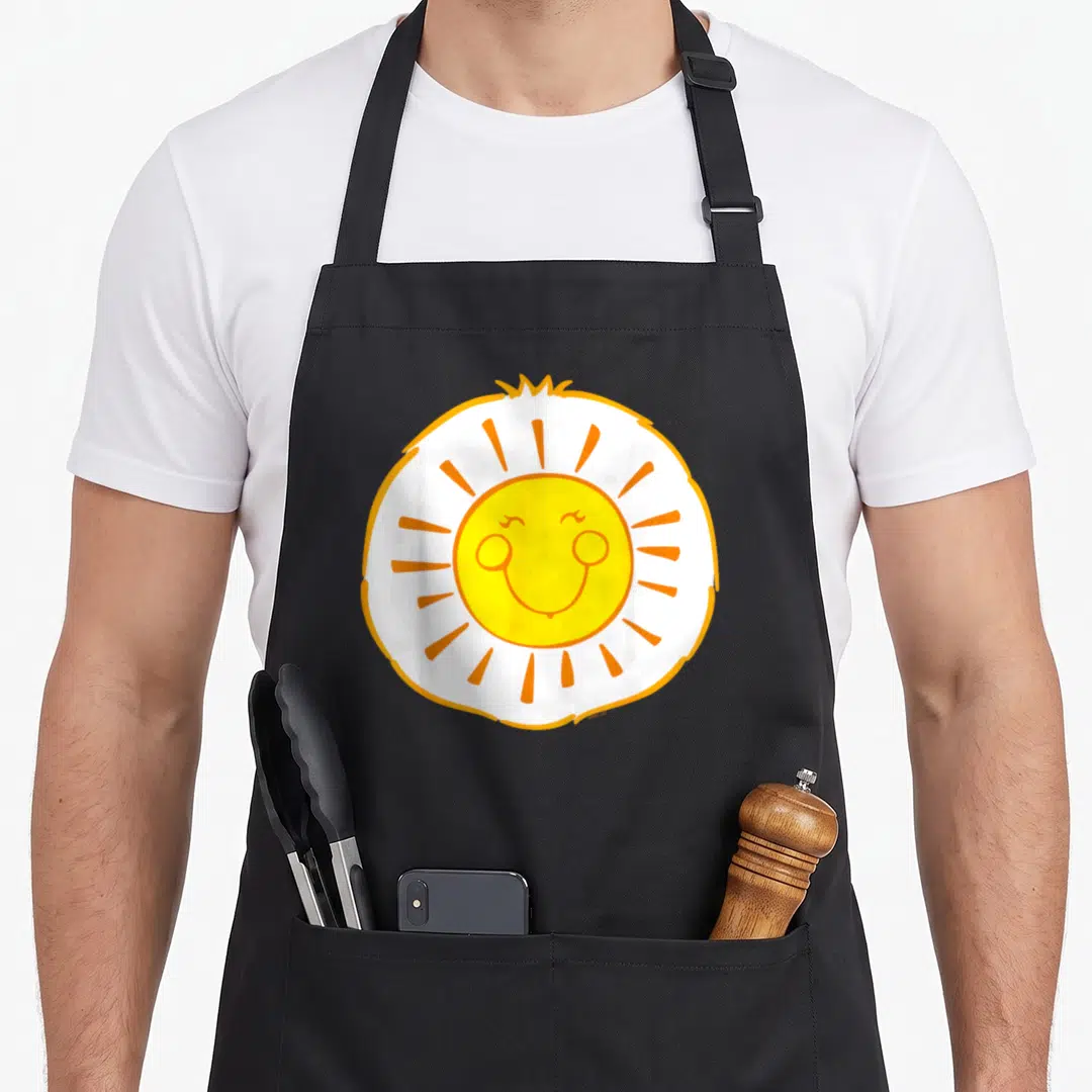 Funshine halloween apron - Cartoon sun with yellow face, white circle, and orange rays on canvas apron — shown on a black cotton canvas apron against a white background