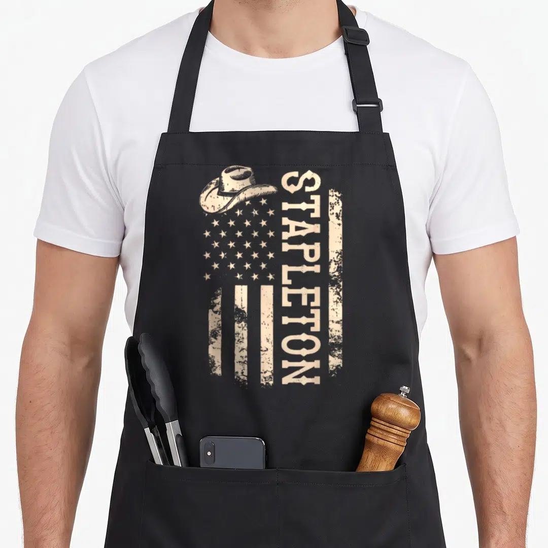 Stapleton 80s apron - Beige distressed US flag with cowboy hat and vertical Stapleton text — shown on a black cotton canvas apron against a white background