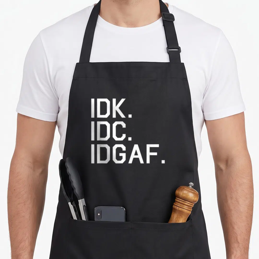 Idc idgaf apron - White stacked text IDK IDC IDGAF typography design — shown on a black cotton canvas apron against a white background