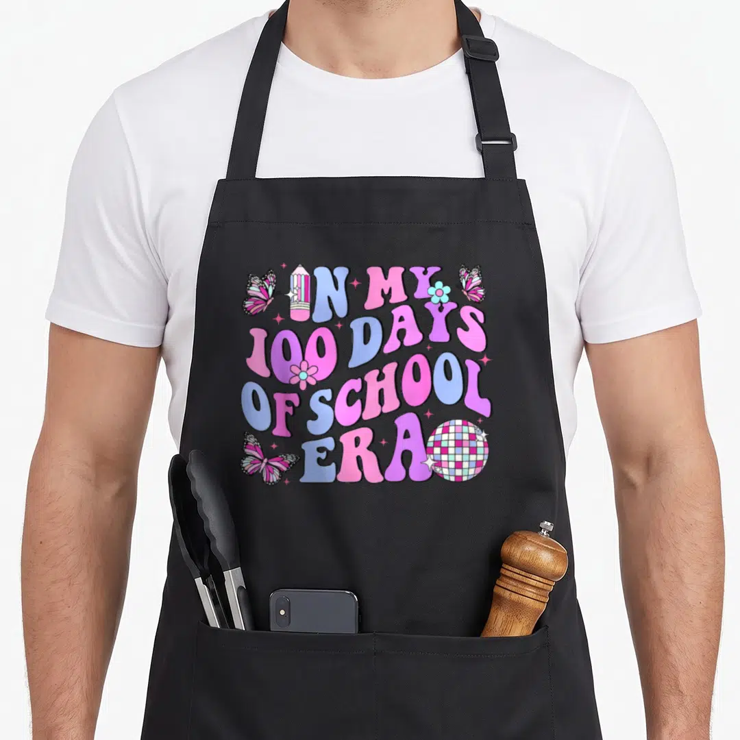 School love kindergarten apron - Bubbly text IN MY 100 DAYS OF SCHOOL ERA with disco ball pencil and butterflies — shown on a black cotton canvas apron against a white background
