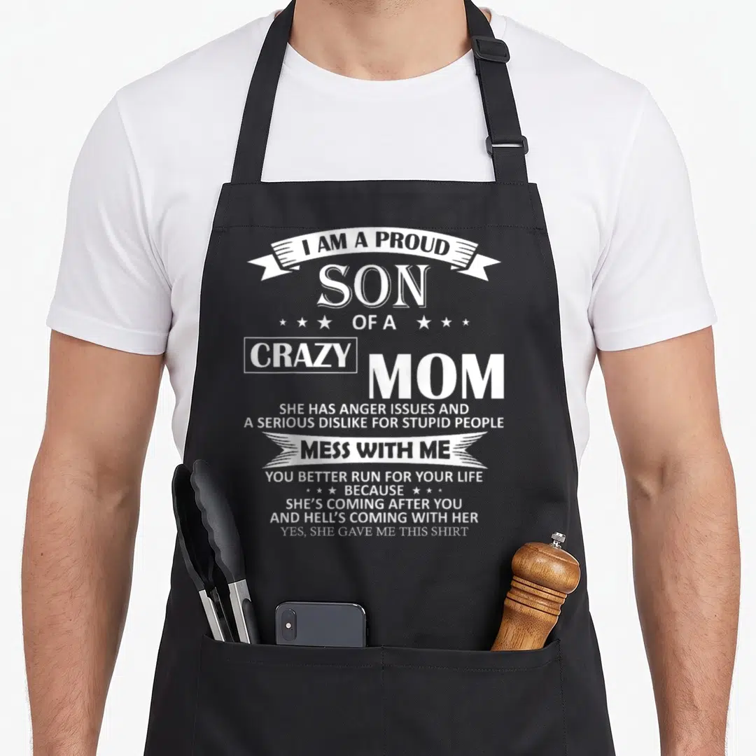 Proud mom and son aprons - White text reading I am a proud son of a crazy mom on black fabric — shown on a black cotton canvas apron against a white background