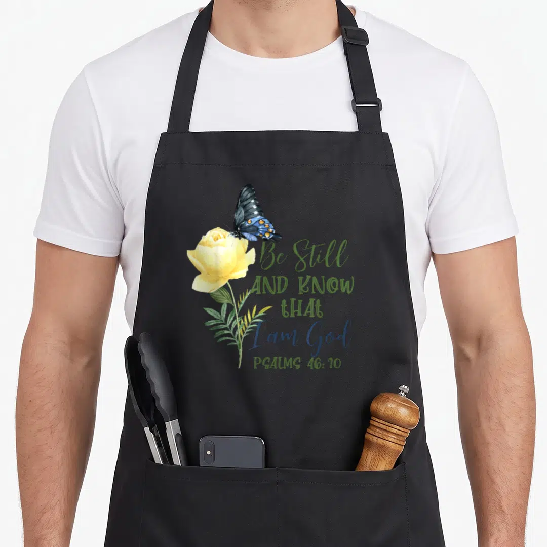 Christian psalm bible verse apron - Yellow rose and blue butterfly with Be Still Psalms 46:10 text in watercolor style — shown on a black cotton canvas apron against a white background