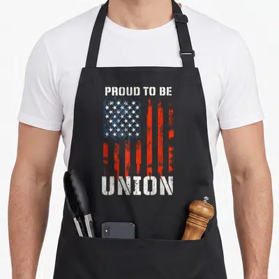 Proud labor union aprons - Distressed USA flag graphic with PROUD TO BE UNION text in red white and blue — shown on a black cotton canvas apron against a white background
