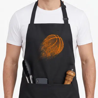 Ball game aprons - Single orange basketball rendered in a distressed splattered dot pattern on black fabric — shown on a black cotton canvas apron against a white background