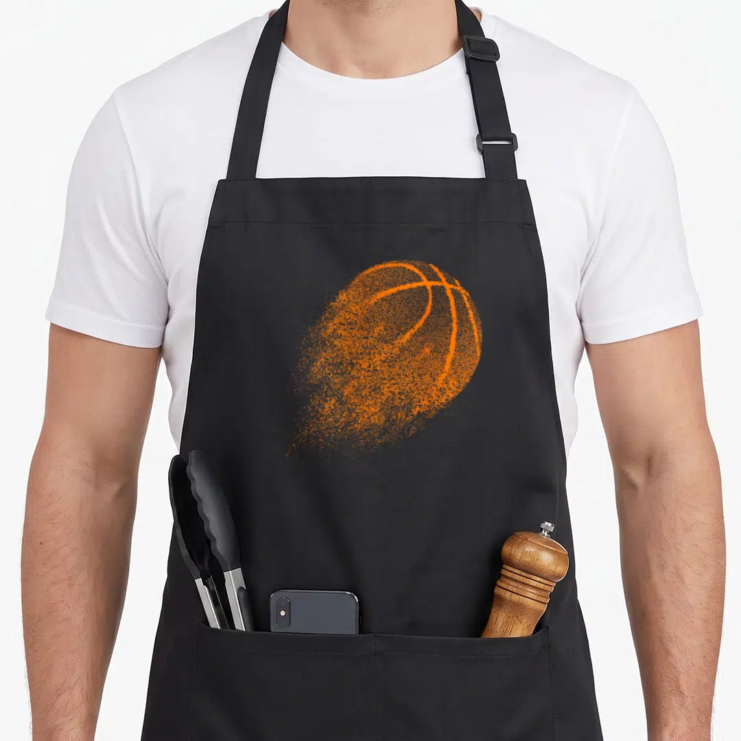 Ball game aprons - Single orange basketball rendered in a distressed splattered dot pattern on black fabric — shown on a black cotton canvas apron against a white background