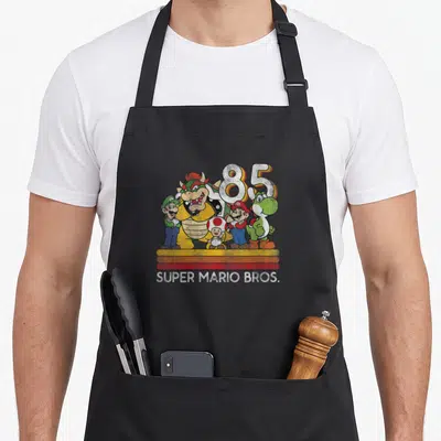 Line character aprons - Bowser Mario Luigi Toad Yoshi grouped before large 85 number with three colored stripes and text — shown on a black cotton canvas apron against a white background