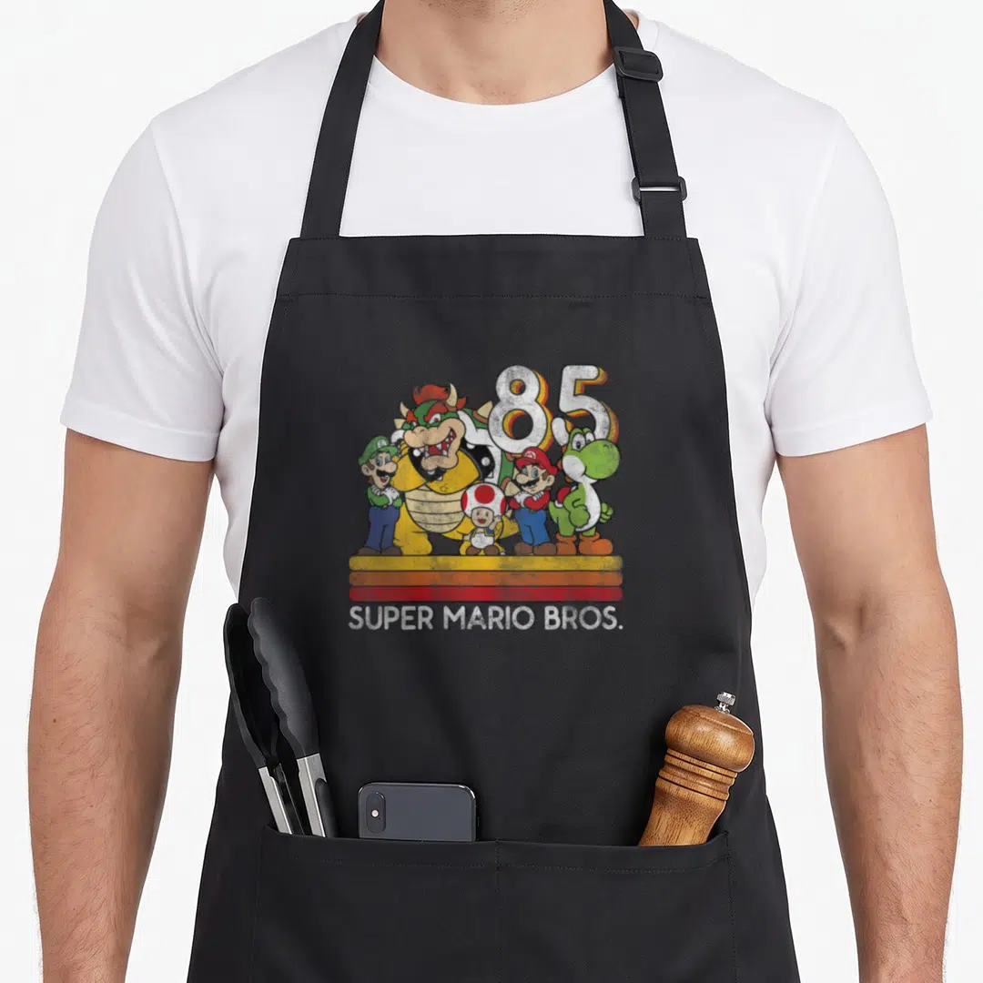 Line character aprons - Bowser Mario Luigi Toad Yoshi grouped before large 85 number with three colored stripes and text — shown on a black cotton canvas apron against a white background