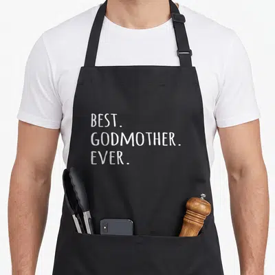 Godmother mother's apron - White stacked text reading BEST GODMOTHER EVER on grey background — shown on a black cotton canvas apron against a white background