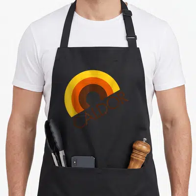 Caldor england apron - Yellow orange brown semi-circle above angled brown CALDOR text in retro style — shown on a black cotton canvas apron against a white background