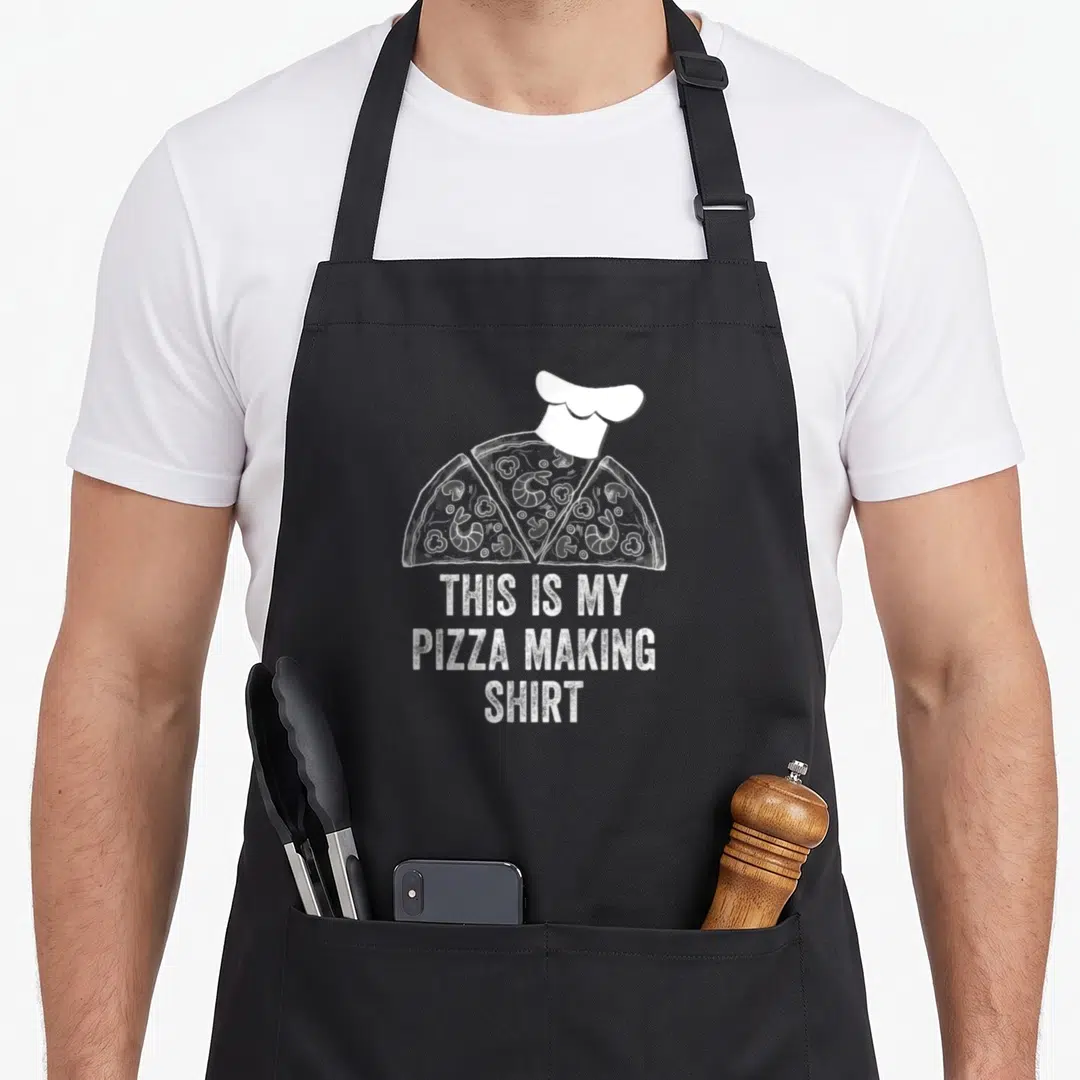Pizza making an apron - Cartoon pizza slices with chef hat and white stacked text reading THIS IS MY PIZZA MAKING SHIRT — shown on a black cotton canvas apron against a white background