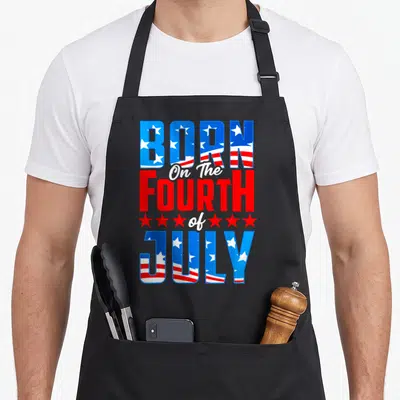 Birthday fourth 4th of july apron - Stacked text BORN On The FOURTH of JULY with flag fills and six red stars in red — shown on a black cotton canvas apron against a white background