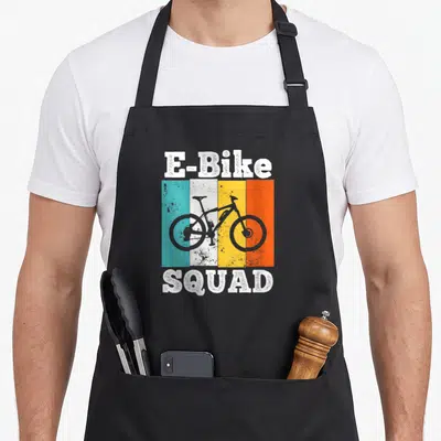 Squad bike apron - Retro E-Bike SQUAD text with bike silhouette over four vertical stripes in teal, white, yellow — shown on a black cotton canvas apron against a white background