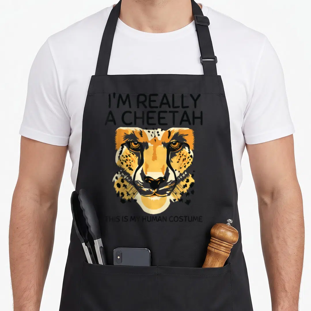 Human cheetah apron - Cartoon cheetah head with I'm Really a Cheetah text in orange, black, and yellow — shown on a black cotton canvas apron against a white background