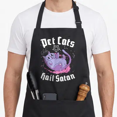 Pet cat apron - Purple cartoon cat lying on pink splash with Pet Cats Hail Satan text and pentagram — shown on a black cotton canvas apron against a white background