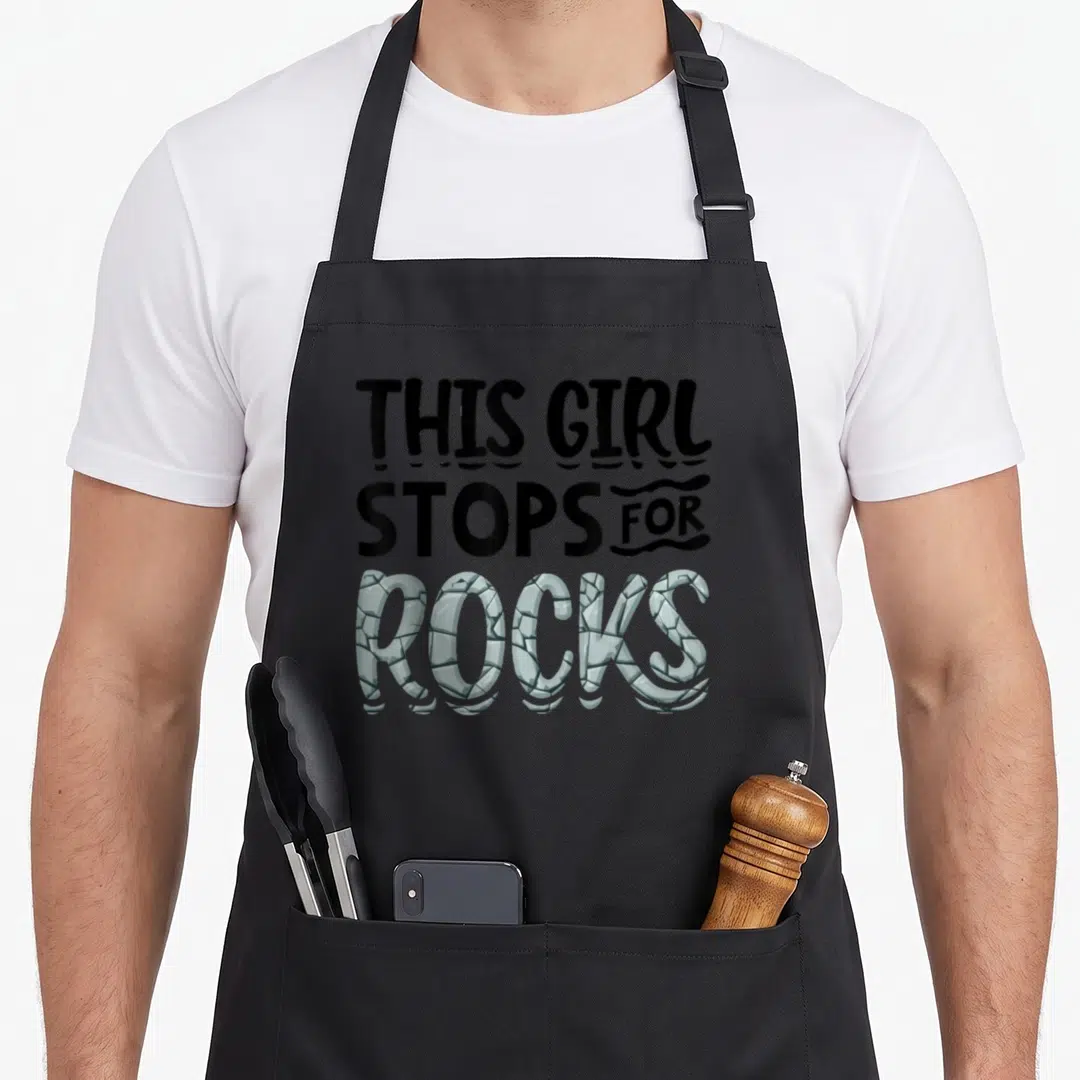 Geologist collecting apron - Stacked text reading this girl stops for rocks with stone texture fill on grey background — shown on a black cotton canvas apron against a white background
