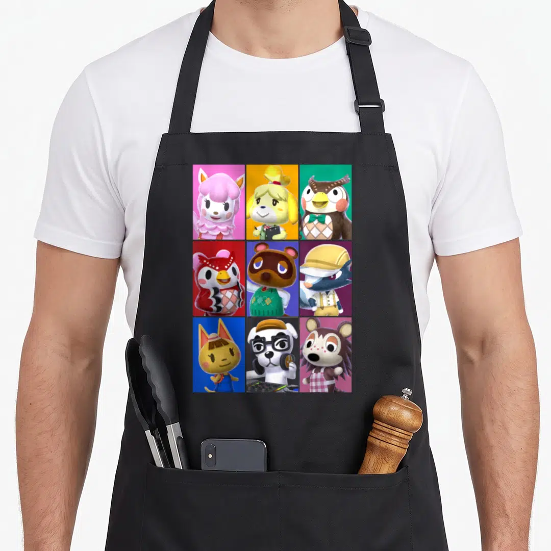 Folk crossover apron - Nine Animal Crossing character portraits in a 3x3 grid with pink, yellow, green, red, and blue — shown on a black cotton canvas apron against a white background