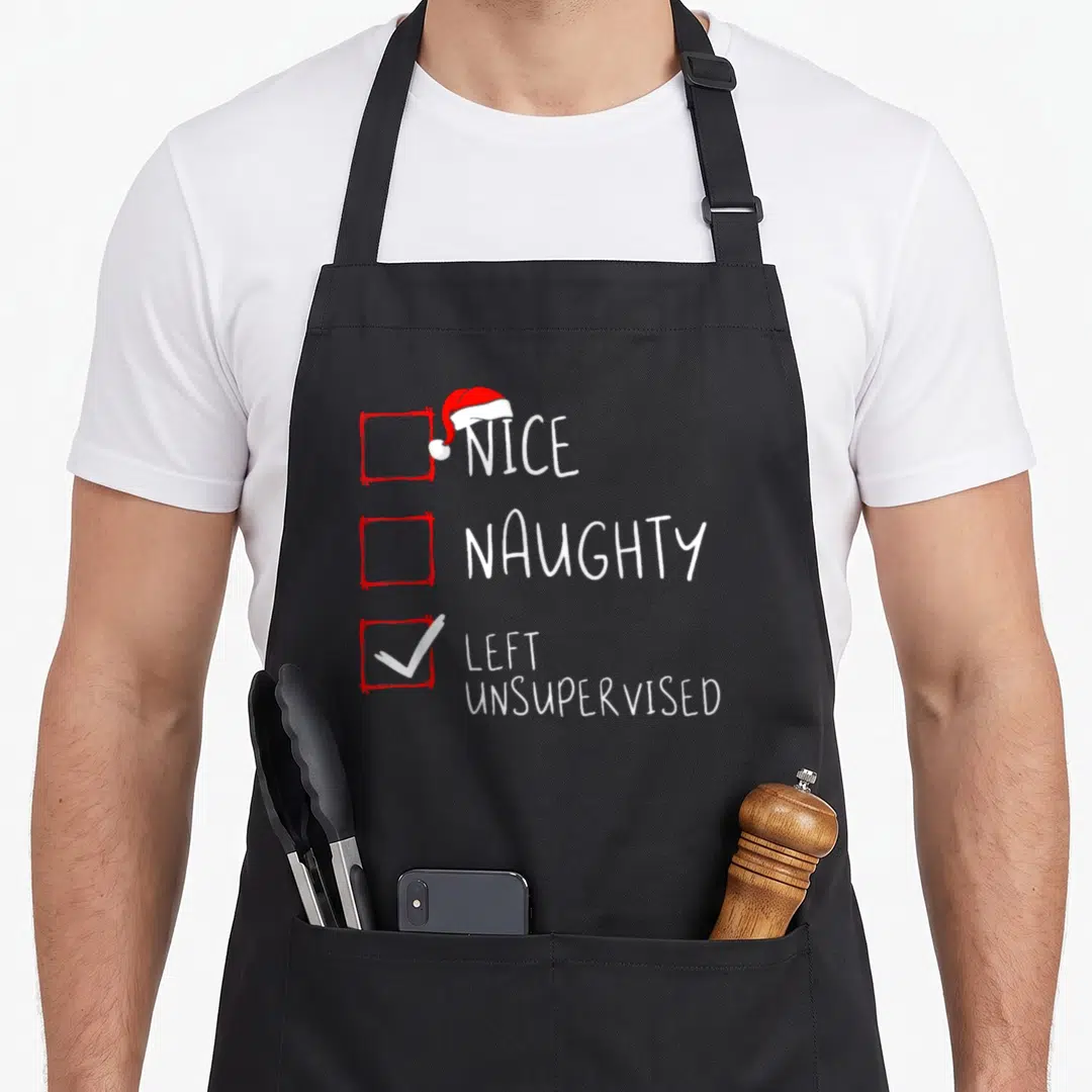Left santa claus apron - Red checkboxes with Santa hat and white checkmark next to Nice Naughty text — shown on a black cotton canvas apron against a white background