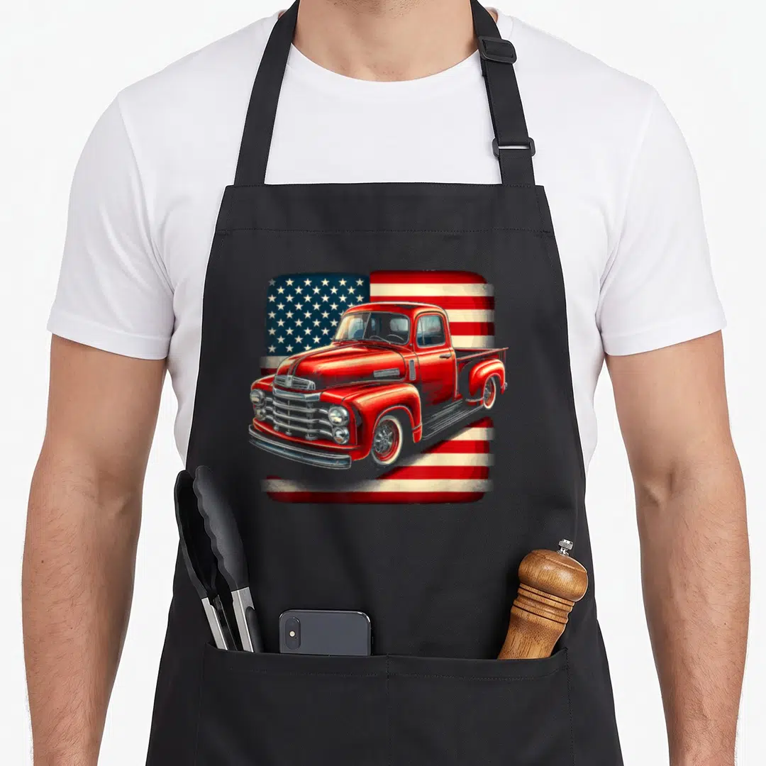 Pickup truck 4th of july apron - Red vintage truck illustration over stylized American flag pattern in red white blue — shown on a black cotton canvas apron against a white background