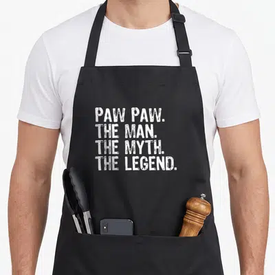 Legend papaya apron - White stacked text reading PAW PAW THE MAN THE MYTH THE LEGEND on dark background — shown on a black cotton canvas apron against a white background