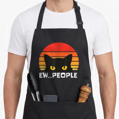Social cat apron - Retro black cat head in front of striped sun with Ew People text below — shown on a black cotton canvas apron against a white background