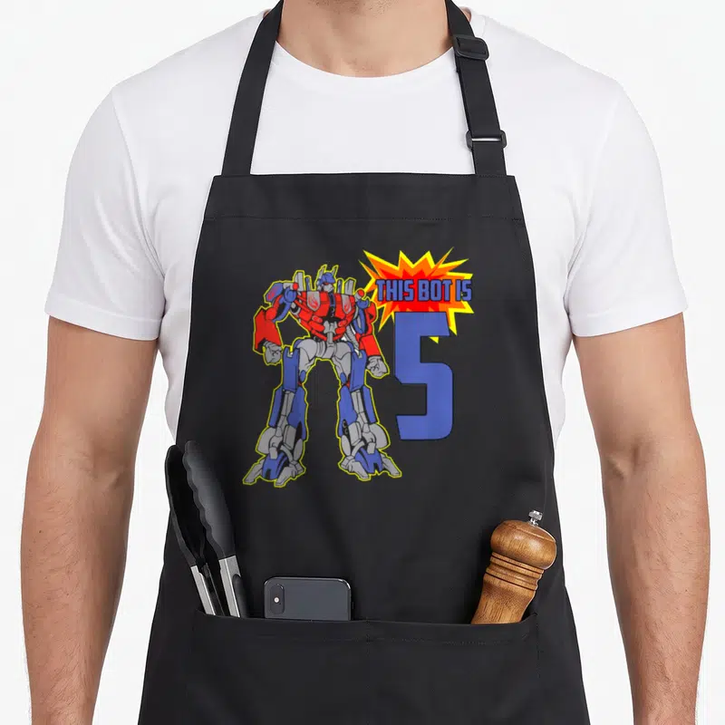 Bot birthday apron - Red blue robot stands beside large blue number 5 with THIS BOT IS text in explosion burst — shown on a black cotton canvas apron against a white background