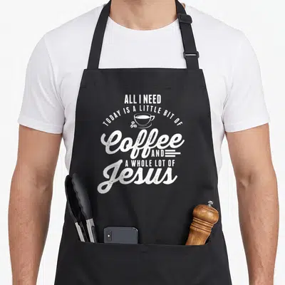 Funny jesus coffee apron - Stacked white text reading All I Need Today Is A Little Bit Of Coffee And A Whole Lot — shown on a black cotton canvas apron against a white background