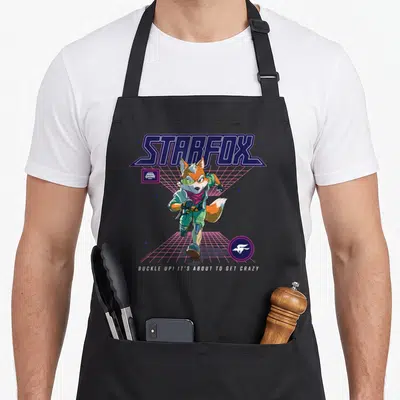 Galaxy novelty apron - Starfox lettering, orange fox on pink grid, buckle up text, retro style — shown on a black cotton canvas apron against a white background