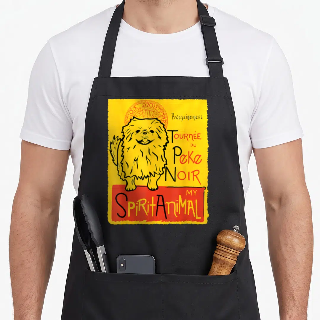 Peke dog apron - Yellow cartoon Pekingese with red halo and French text Prochainement Tournée du Peke Noir My Spirit — shown on a black cotton canvas apron against a white background