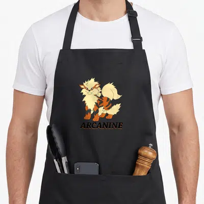 Arcanine trend apron - Cartoon dog standing over black text ARCANINE in orange and cream colors — shown on a black cotton canvas apron against a white background
