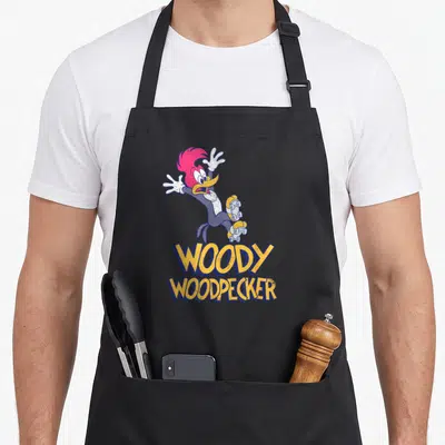 Falling woodpecker apron - Woody Woodpecker character in yellow blue and red above stacked text — shown on a black cotton canvas apron against a white background