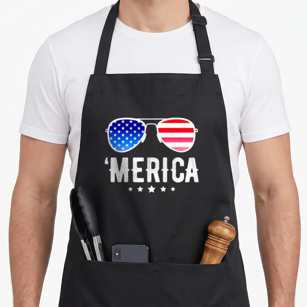 Fourth american flag apron - Aviator sunglasses with US flag lenses above distressed 'MERICA text and five stars — shown on a black cotton canvas apron against a white background