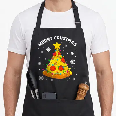 Crustmas merry christmas apron - Pizza Christmas tree with MERRY CRUSTMAS text, yellow star, red pepperoni, and blue — shown on a black cotton canvas apron against a white background