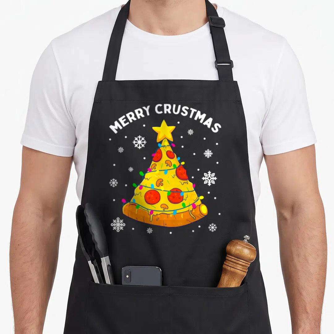 Crustmas merry christmas apron - Pizza Christmas tree with MERRY CRUSTMAS text, yellow star, red pepperoni, and blue — shown on a black cotton canvas apron against a white background