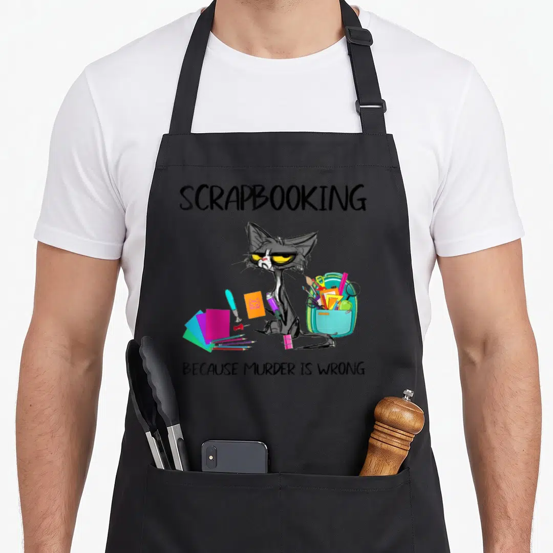 Scrapbooking cat apron - Grey cartoon cat with teal backpack and pink paper under text Because Murder Is Wrong — shown on a black cotton canvas apron against a white background