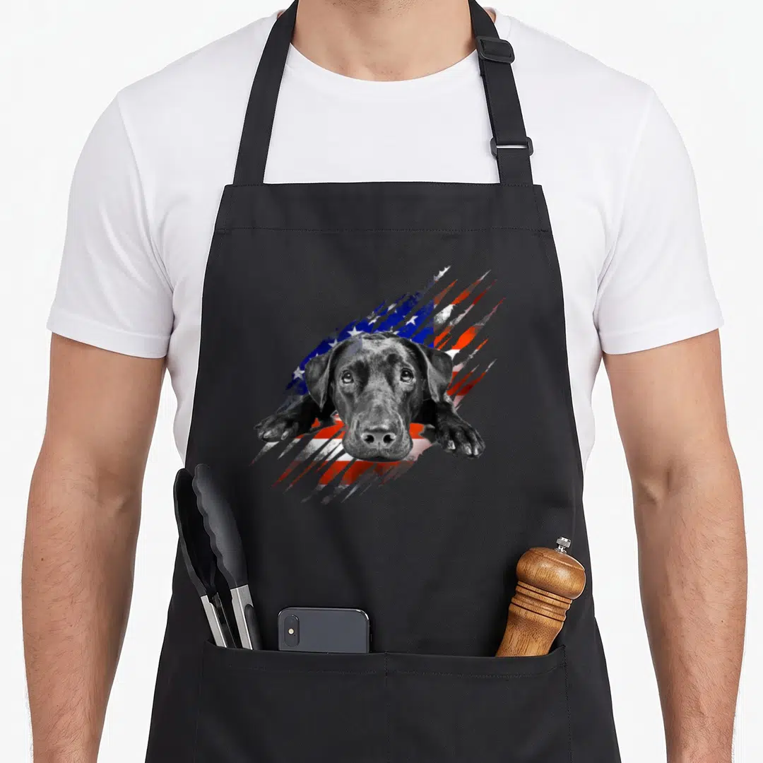 Labrador bird aprons - Black lab dog head and paws over distressed USA flag stripes — shown on a black cotton canvas apron against a white background