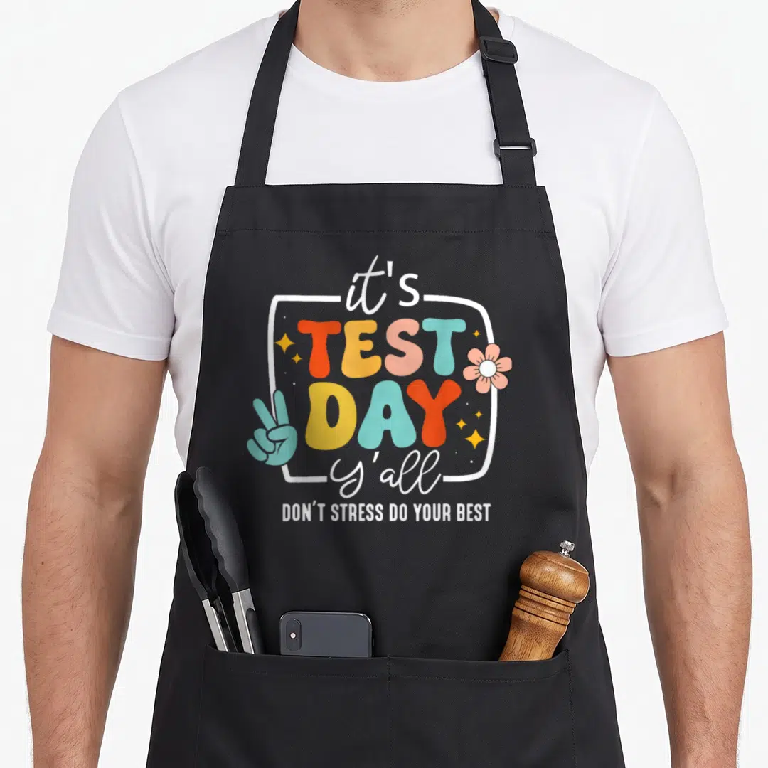 Test yall teacher apron - Colorful bubble text reading it's TEST DAY y'all with peace sign and flower in white frame — shown on a black cotton canvas apron against a white background