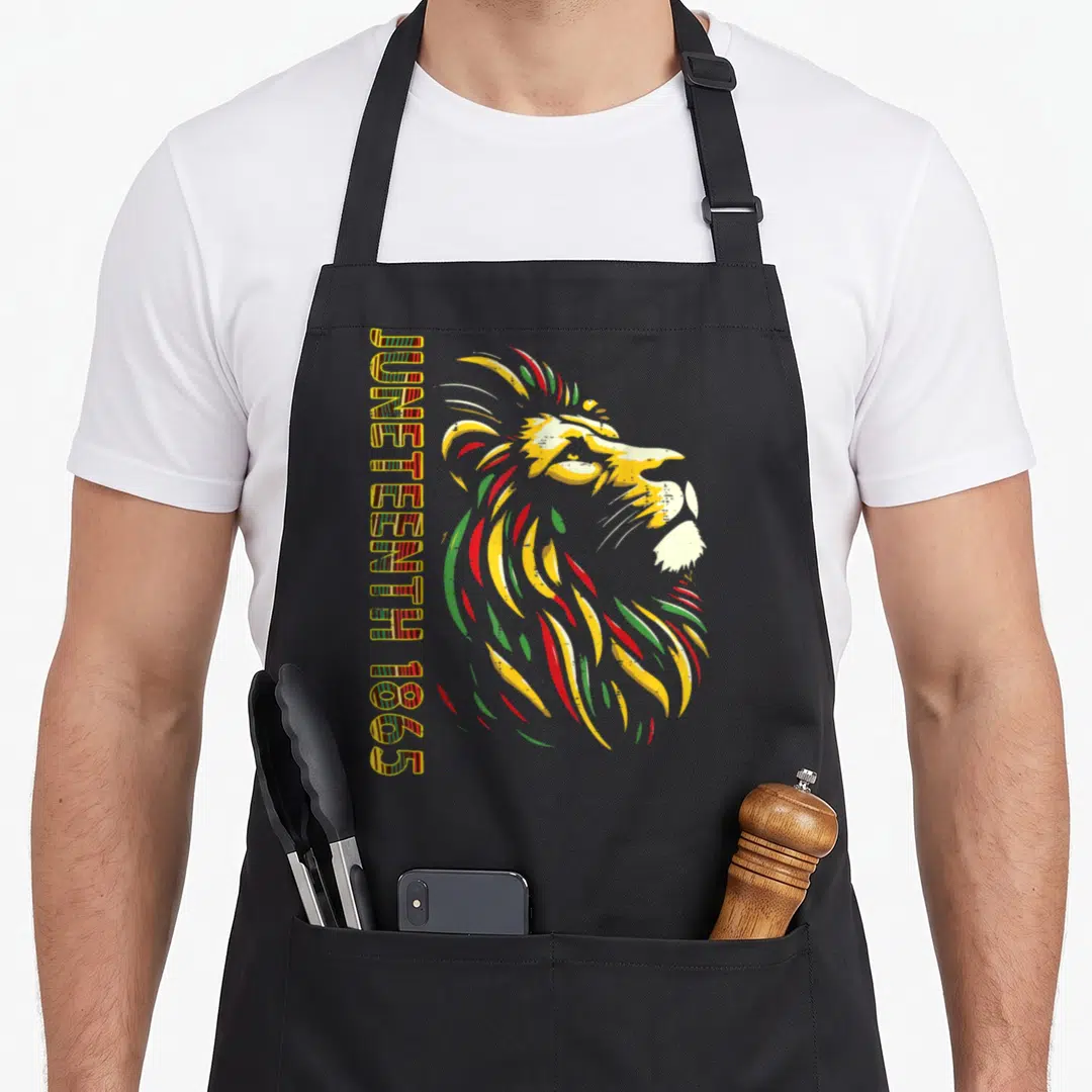 Lion african apron - Vertical JUNETEENTH 1865 text next to a multi-colored cartoon lion head — shown on a black cotton canvas apron against a white background