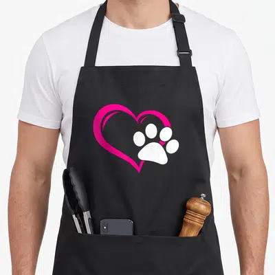 Puppy cat apron - Pink heart outline with overlapping white paw print graphic — shown on a black cotton canvas apron against a white background