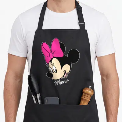Cute face friends apron - Minnie Mouse head with pink bow and white script text — shown on a black cotton canvas apron against a white background