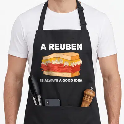 Alway reuben apron - Cartoon reuben sandwich with white text reading A REUBEN IS ALWAYS A GOOD IDEA — shown on a black cotton canvas apron against a white background