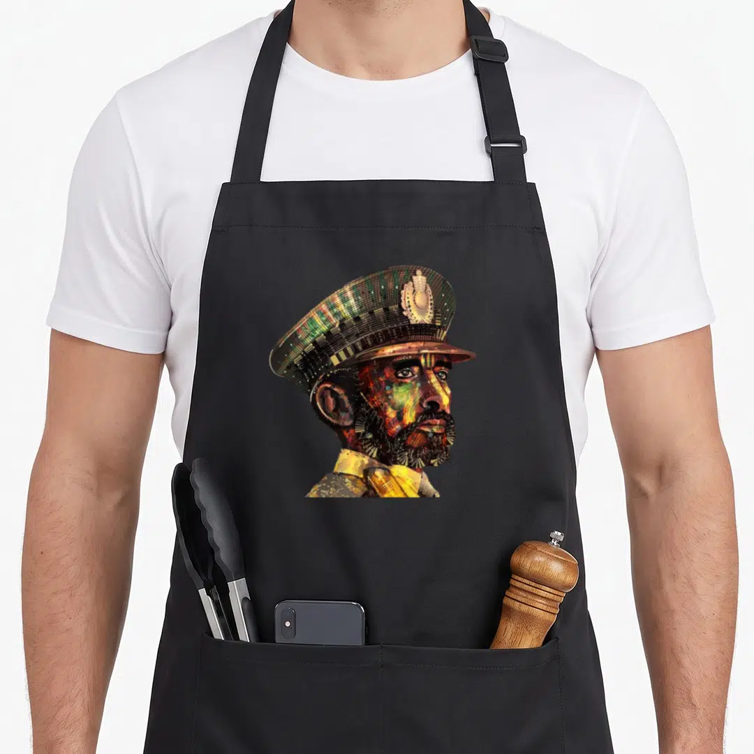 Visionary ethiopian apron - Pixel mosaic portrait of a man in a peaked cap using yellow green red and black colors — shown on a black cotton canvas apron against a white background