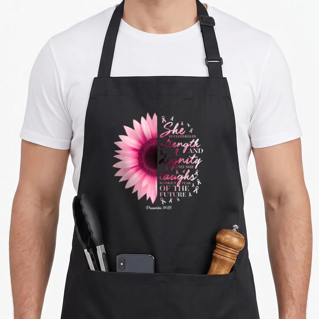 Proverb breast cancer awareness aprons - Pink flower half-circle next to Proverbs 31:25 text and scattered pink ribbons — shown on a black cotton canvas apron against a white background