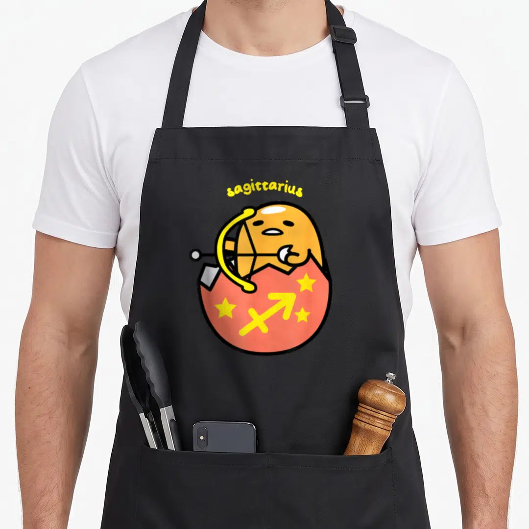 Sagittarius gudetama apron - Orange egg character holding bow in cracked red shell with Sagittarius symbol and yellow — shown on a black cotton canvas apron against a white background