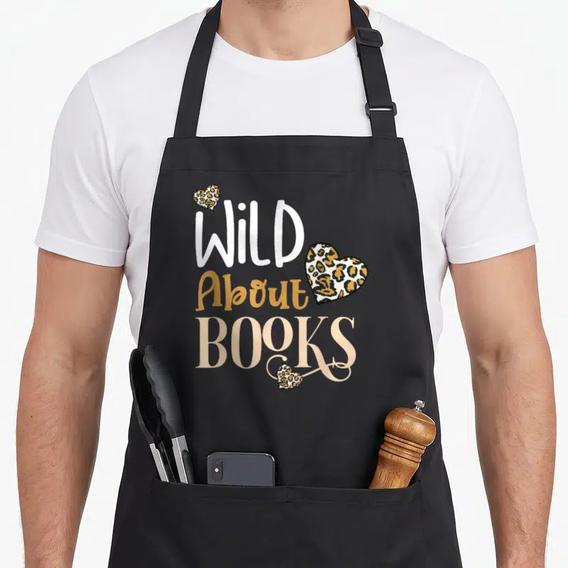 Wild leopard apron - Stacked Wild About Books text with three leopard print hearts in white gold beige — shown on a black cotton canvas apron against a white background