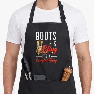 Bling western apron - Decorated cowboy boot with BOOTS & Bling It's A Cowgirl Thing text — shown on a black cotton canvas apron against a white background