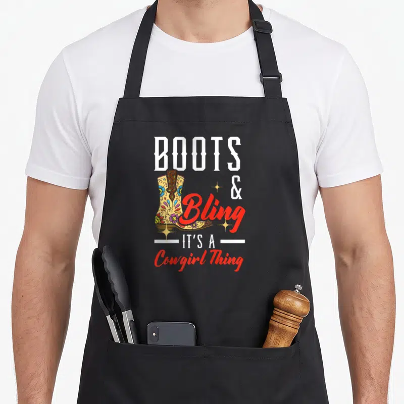Bling western apron - Decorated cowboy boot with BOOTS & Bling It's A Cowgirl Thing text — shown on a black cotton canvas apron against a white background