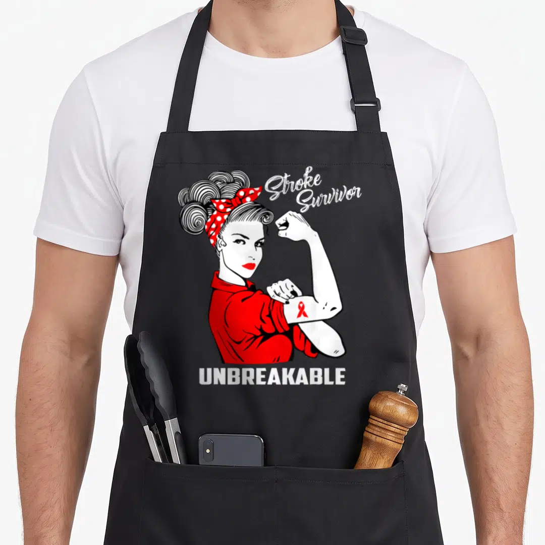 Survivor stroke awareness apron - Cartoon woman flexing arm with red ribbon and text Stroke Survivor Unbreakable — shown on a black cotton canvas apron against a white background