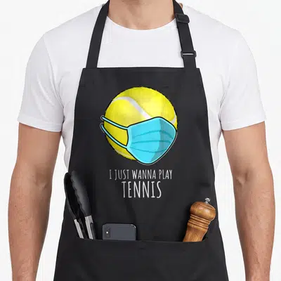 Player tennis apron - Yellow tennis ball wearing a blue surgical face mask above white text I Just Wanna Play Tennis — shown on a black cotton canvas apron against a white background